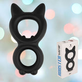 The Velv'Or Rooster Kalf Dual-Ring Cat-Like Cock Ring, made of black silicone and featuring ears, a face, and an inner circular opening, is showcased next to a white Velv'Or branded box against a blurred background of pastel-colored lights.